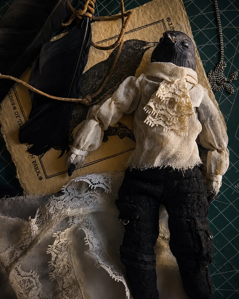 An art doll resting among lace, feathers and materials