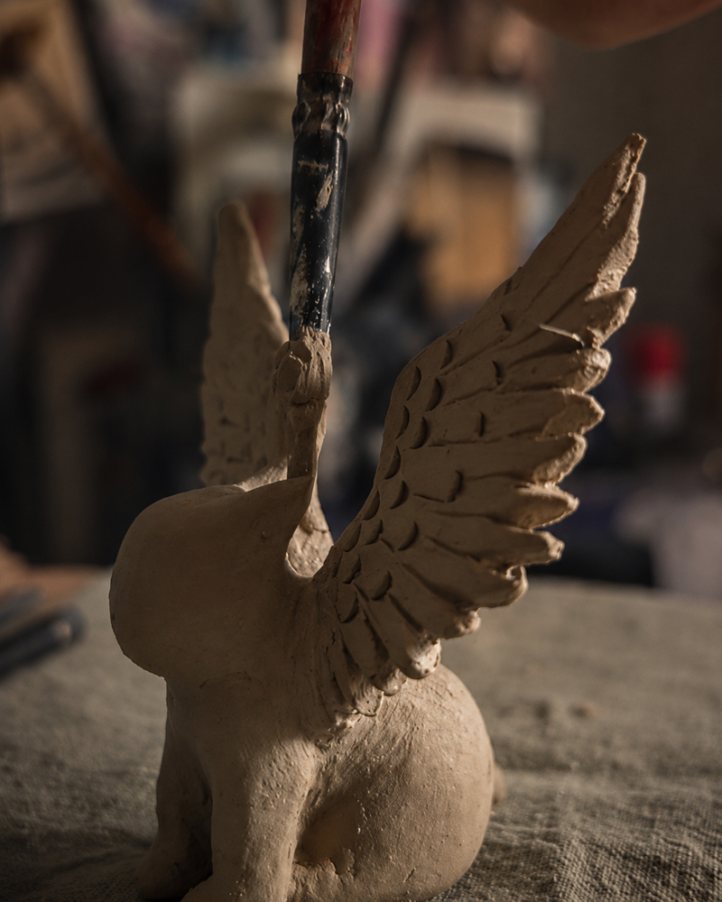 Refining a winged clay figure by hand