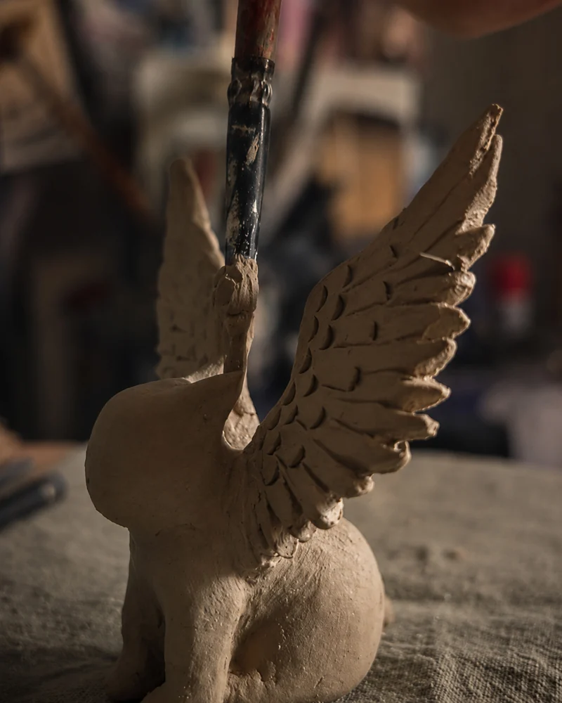 Refining a winged clay figure by hand